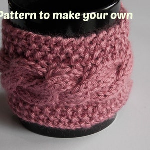 May include: A dusty rose-colored knitted mug cozy with a cable knit design. The cozy is wrapped around a black mug. The text "Pattern to make your own" is at the top of the image.