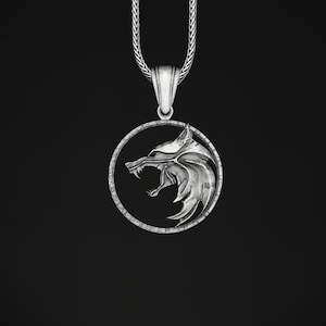 Può includere: Una collana d'argento con un ciondolo che presenta una testa di lupo in un cerchio. La testa di lupo è dettagliata e ha un'espressione feroce.