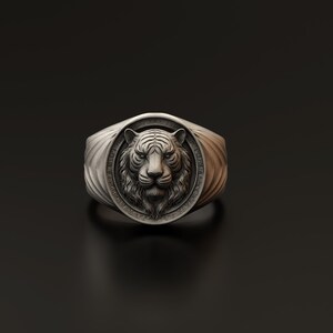 Puede incluir: Un anillo de plata con un diseño detallado de cabeza de tigre. La cara del tigre está en el centro del anillo, con una banda texturizada.