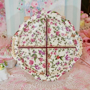 May include: A white ceramic divided serving dish with a floral pattern in shades of pink, purple, and green. The dish has a scalloped edge and pearl-like accents around the rim.
