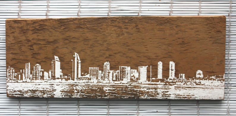May include: A wooden sign with a white silhouette of a city skyline. The sign has a rustic brown color and a weathered texture.