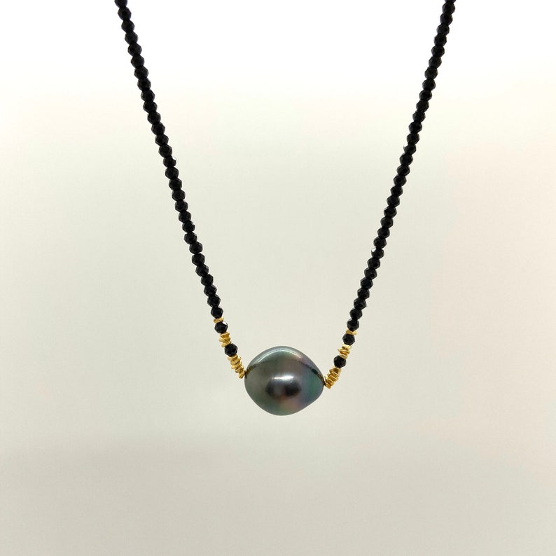 May include: A black pearl necklace with a single large, dark grey pearl pendant. The necklace is made of small black beads and gold spacers.
