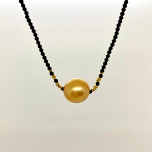 May include: A gold pearl necklace with black beads. The pearl is large and round.