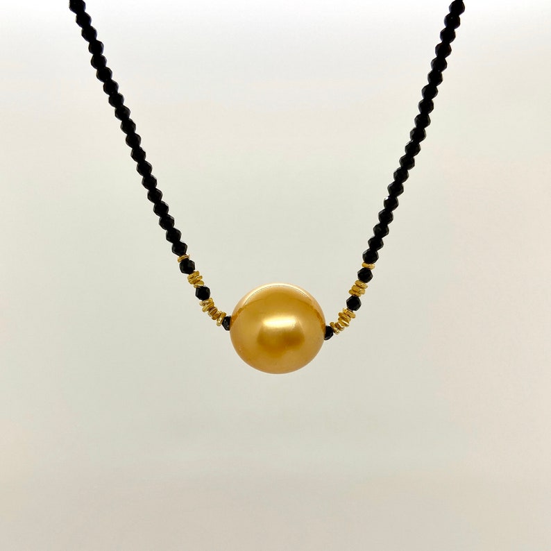May include: A gold pearl necklace with black beads. The pearl is large and round.