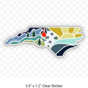 K&ouml;nnte beinhalten: Ein transparenter Aufkleber mit einer farbenfrohen Illustration des Bundesstaates North Carolina. Das Design beinhaltet einen Kardinal, Berge, einen Sonnenaufgang und Blumen. Der Aufkleber ist 3,0 Zoll mal 1,2 Zoll gro&szlig;.