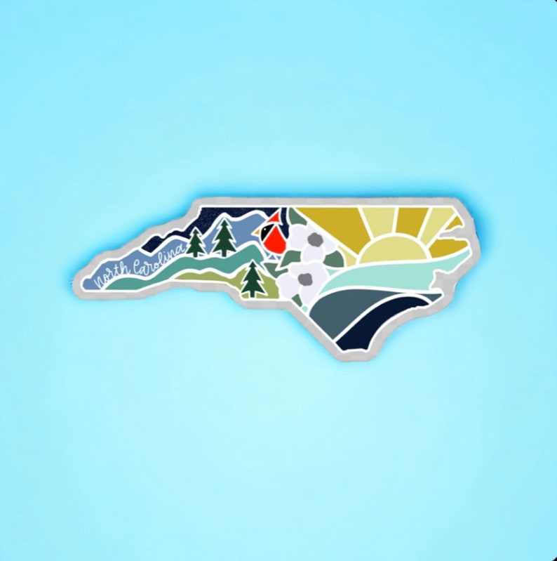 K&ouml;nnte beinhalten: Eine graue Umrandung des Bundesstaates North Carolina mit einer bunten Illustration im Inneren. Die Illustration zeigt einen Kardinal, Berge, einen Sonnenaufgang und einen Fluss. Der Text "North Carolina" ist in Kursivschrift auf der linken Seite der Umrandung geschrieben.