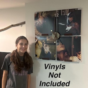 May include: A clock made from four vinyl records with a wooden clock face and hands. The clock is mounted on a wall with brown brackets. The text "Vinyl's Not Included" is written below the clock.