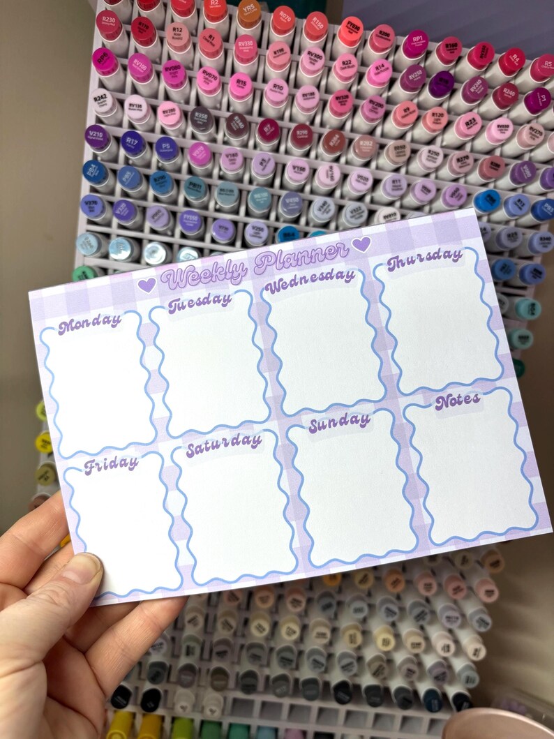 May include: A weekly planner with a light purple gingham border and wavy blue edges. The planner has sections for each day of the week, plus a notes section. The text "Weekly Planner" is at the top, with the days of the week labeled below.