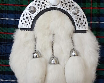 May include: White fur sporran with a silver ornate metal buckle and three silver tassels. The sporran is on a green, blue, and white plaid fabric.