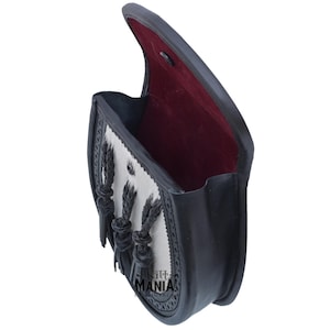May include: A black leather sporran with a white fur flap and black braided tassels. The sporran is open and the inside is lined with red fabric.