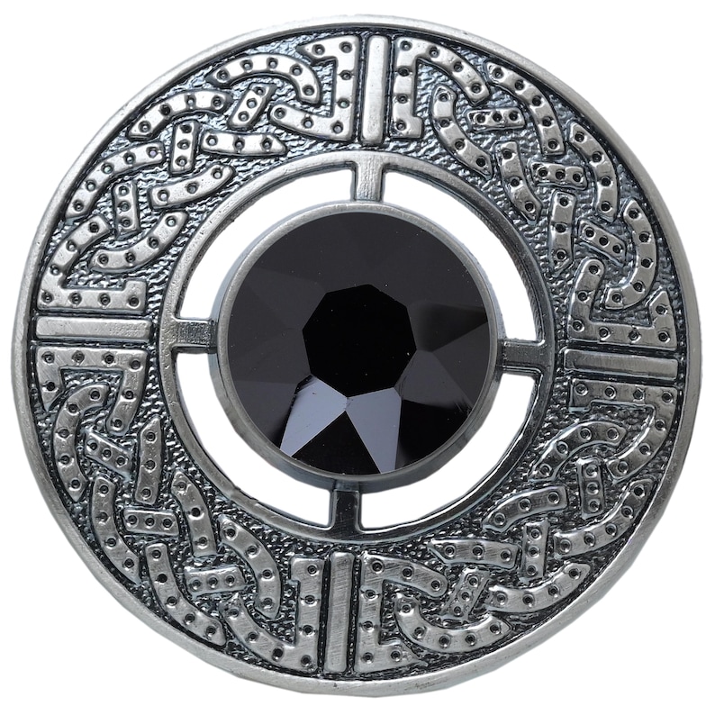 Puede incluir: Un broche redondo plateado con una gema negra central. El broche presenta un intrincado dise&ntilde;o de nudo celta alrededor de la gema y el borde exterior. El dise&ntilde;o es detallado y sim&eacute;trico, con un acabado pulido.