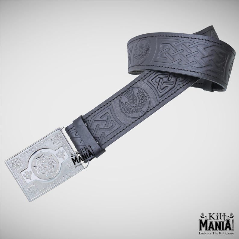 May include: A black leather belt with embossed Celtic knot and thistle designs. The silver buckle features a central emblem and floral details. The belt is from Kilt Mania.