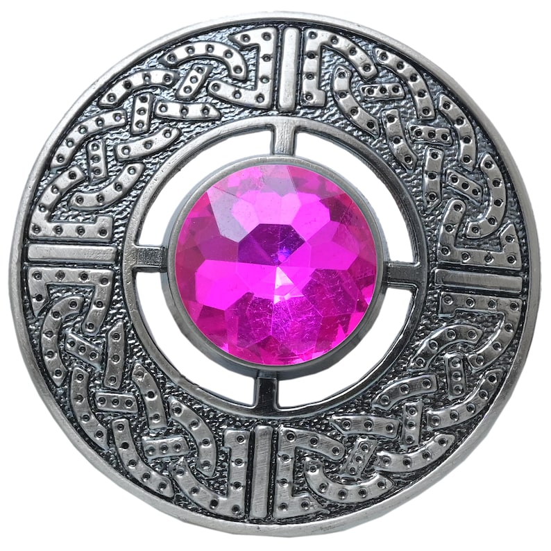 Puede incluir: Broche plateado con dise&ntilde;o de nudo celta y una gran gema rosa facetada en el centro. El broche circular presenta intrincados detalles en los bordes.