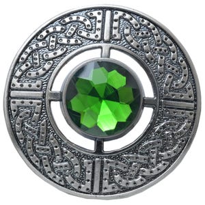 Puede incluir: Broche circular plateado con dise&ntilde;o de nudo celta. El broche presenta una gran gema verde esmeralda facetada en el centro. El intrincado trabajo en metal rodea la gema, creando un accesorio detallado y decorativo.