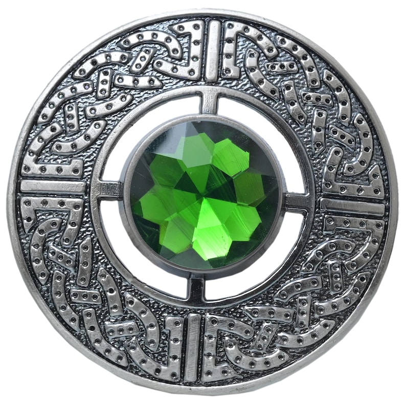 Puede incluir: Broche circular plateado con dise&ntilde;o de nudo celta. El broche presenta una gran gema verde esmeralda facetada en el centro. El intrincado trabajo en metal rodea la gema, creando un accesorio detallado y decorativo.