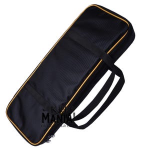 Puede incluir: Estuche de transporte negro con cremallera y ribetes dorados. El estuche tiene dos asas y una correa para el hombro.