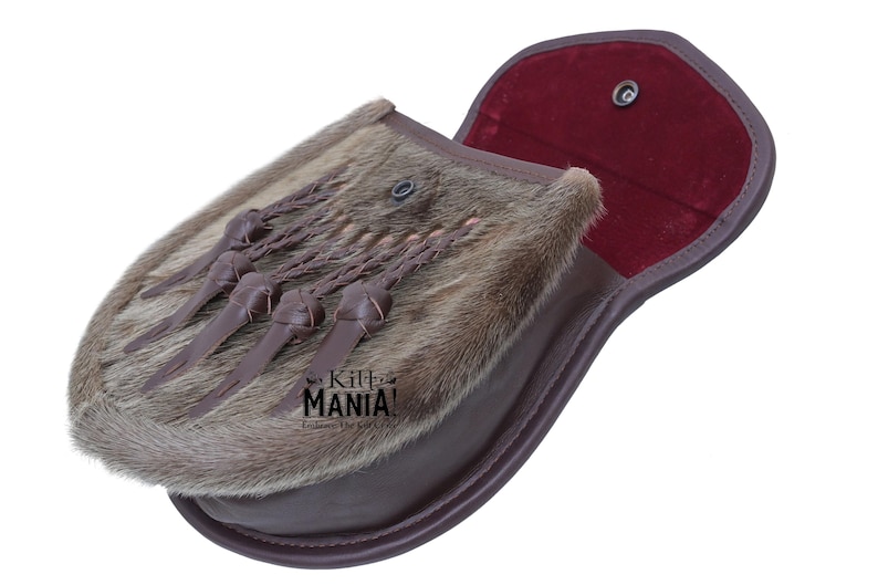 May include: A brown leather sporran with a fur flap and a red velvet lining. The sporran has a braided strap with tassels and a metal snap closure.