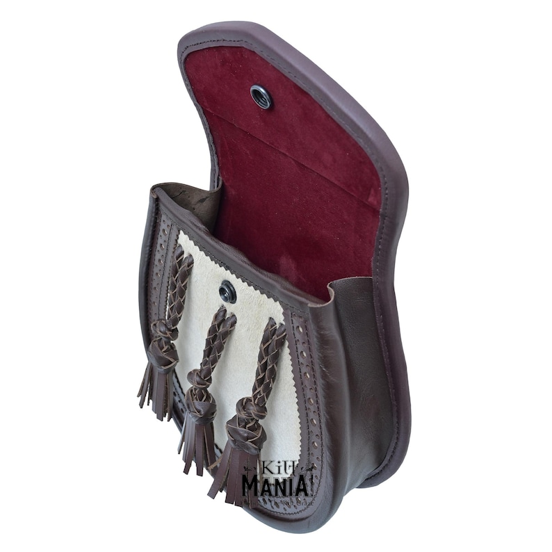 May include: A brown leather bag with a white leather flap and three braided leather tassels. The bag is open and the inside is lined with red fabric.