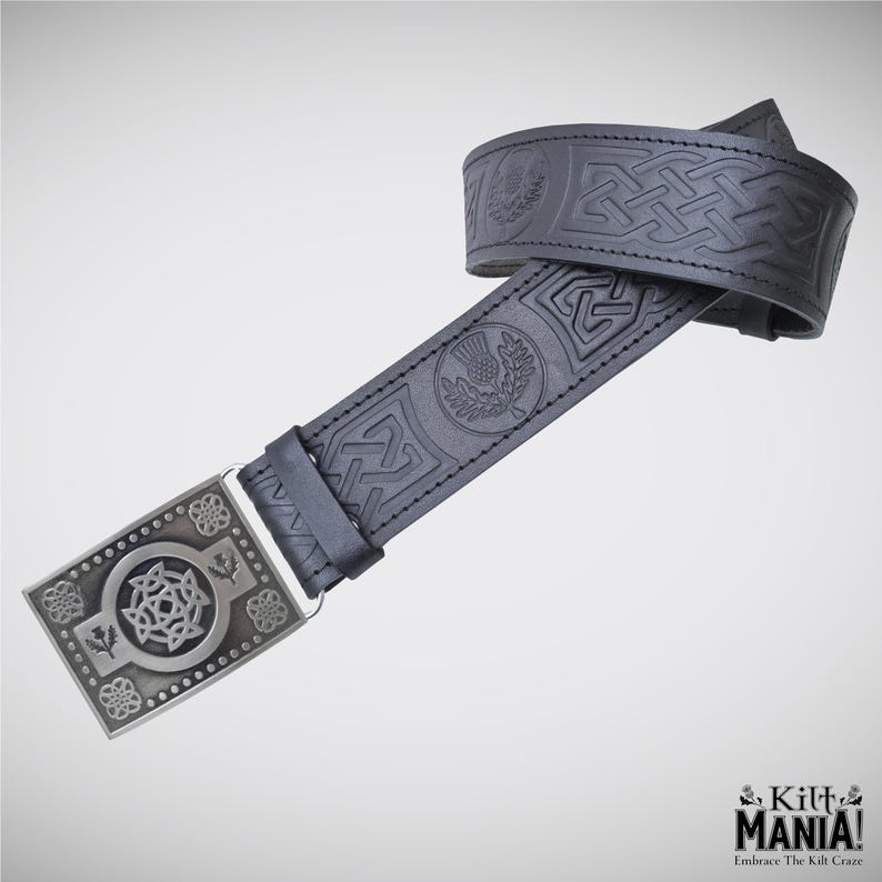 May include: Black leather belt with embossed Celtic knot and thistle designs. The belt features a silver-colored rectangular buckle with intricate patterns. The belt is designed for kilts and has the text "Kilt Mania! Embrace The Kilt Craze!"