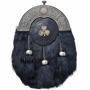 Puede incluir: Un sporran de piel negra con un dise&ntilde;o celta plateado en la parte superior. El sporran tiene una parte delantera de cuero negro con un emblema de tr&eacute;bol dorado. Cadenas y borlas plateadas cuelgan de la parte inferior. El texto "Kilt MANIA!" es visible.