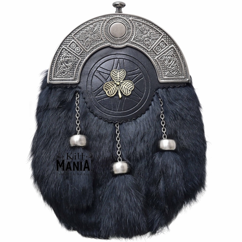 Puede incluir: Un sporran de piel negra con un dise&ntilde;o celta plateado en la parte superior. El sporran tiene una parte delantera de cuero negro con un emblema de tr&eacute;bol dorado. Cadenas y borlas plateadas cuelgan de la parte inferior. El texto "Kilt MANIA!" es visible.