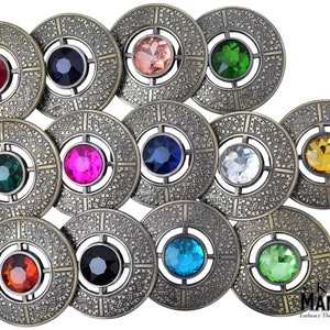 May include: Twelve antique gold-toned brooches with different colored gemstones in the center. Each brooch has a Celtic knot design around the gemstone.