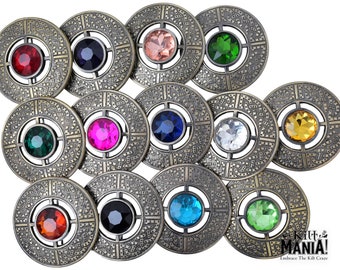 Puede incluir: Doce broches de color dorado antiguo con gemas de colores diferentes en el centro. Cada broche tiene un diseño de nudo celta alrededor de la gema.