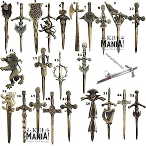 May include: A collection of 23 gold-toned kilt pins with various designs, including swords, thistles, and animals. The pins are numbered 1 through 23. The text "Kilt MANIA! Embrace The Kilt Craze" appears twice on the image.