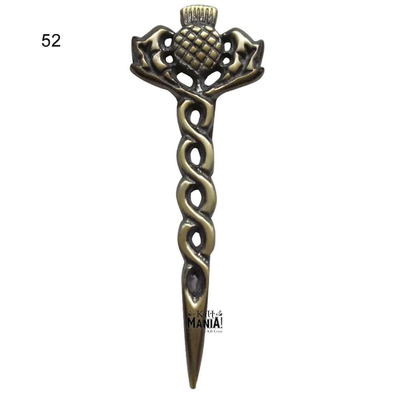 May include: A gold-toned metal kilt pin with a thistle design. The pin is shaped like a sword with a twisted handle and a pointed tip. The thistle is detailed with a textured surface and a small stem.