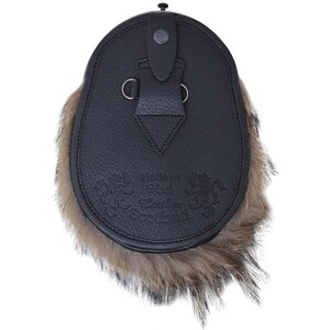 May include: Black leather sporran with a brown fur trim. The sporran has a strap with a buckle and two metal rings. The sporran is decorated with an embossed design that says "Chief of the Clan Scotland".