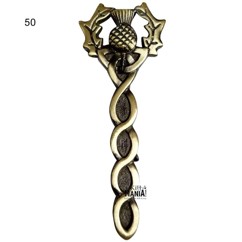 May include: A gold-colored metal pin with a Celtic knot design and a thistle in the center. The thistle is surrounded by a wreath of leaves. The pin is about 5 inches long.