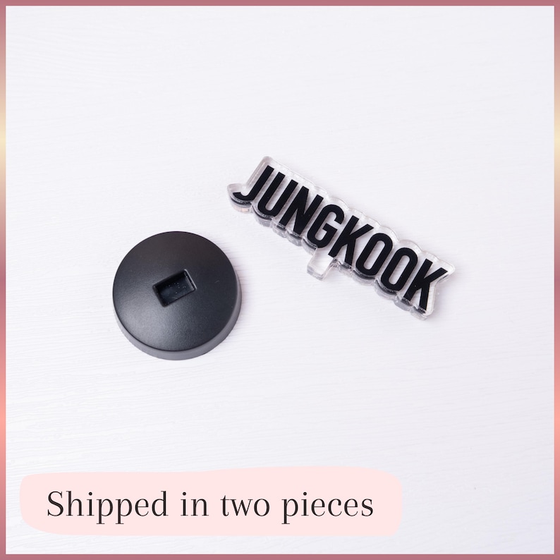 May include: A black circular base with a rectangular slot and a clear acrylic piece featuring the black text JUNGKOOK in a bold, sans-serif font. The two separate components are displayed together, showing the base and the nameplate.