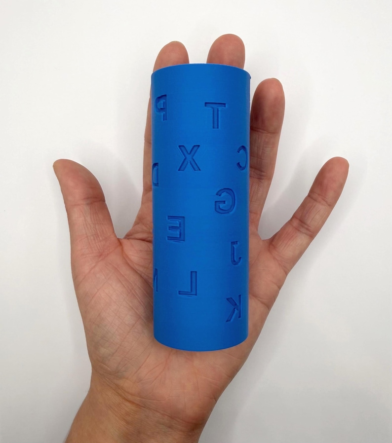 Op de afbeelding: Een felblauwe cilindrische roller met in reli&euml;f aangebrachte letters en cijfers op het oppervlak. De zichtbare tekens zijn onder andere P, T, X, C, D, G, E, 1, M, L en K, die in het materiaal zijn gedrukt. Het object heeft een gladde, matte afwerking.