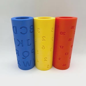May include: Three cylindrical molds standing upright. The blue mold features embossed uppercase letters of the alphabet. The yellow mold displays embossed numbers. The orange mold features embossed numbers in a different sequence and arrangement.
