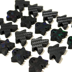 May include: A collection of small, black, ghost-shaped buttons arranged in a grid. Each button features a distinct surface texture, including chevron patterns, holographic squares, and iridescent green or blue flecks, with two small holes for attachment.