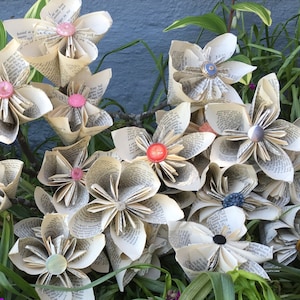 Origami di carta a forma di fiore: pagine di libri bianchi antichi fatti a mano con scritte nere, steli di rami e centro del bottone di GmaJanisew