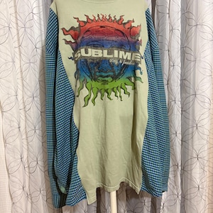 May include: A long-sleeve shirt with a light green center panel and blue and green gingham side panels. The front features a graphic of a rainbow-colored sun with the text SUBLIME and 100% to freedom printed across the center.