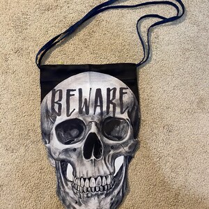 May include: Black drawstring bag with a skull graphic and the word "BEWARE" printed on it.