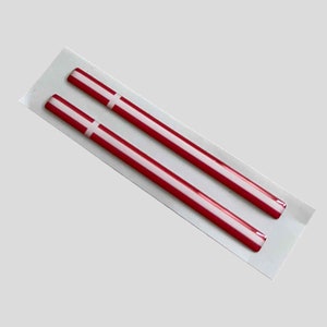 Könnte beinhalten: Zwei rote und weiße dänische Flaggenaufkleber. Die Aufkleber sind dünn und rechteckig mit einem weißen Kreuz auf rotem Hintergrund.