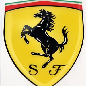 Pode incluir: Um emblema amarelo em forma de escudo com um cavalo preto empinado e as letras "SF" em preto.