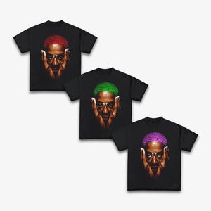 Puede incluir: Tres camisetas negras con un retrato de una persona con el pelo de diferentes colores. La primera camiseta presenta el pelo rojo, la segunda el pelo verde y la tercera el pelo morado.