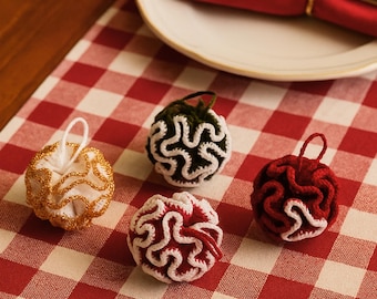 May include: Four spherical crochet ornaments with ruffled edges. One is white with gold trim, one is dark green with white trim, one is red with white trim, and one is dark red with white trim. Each has a small loop for hanging at the top.
