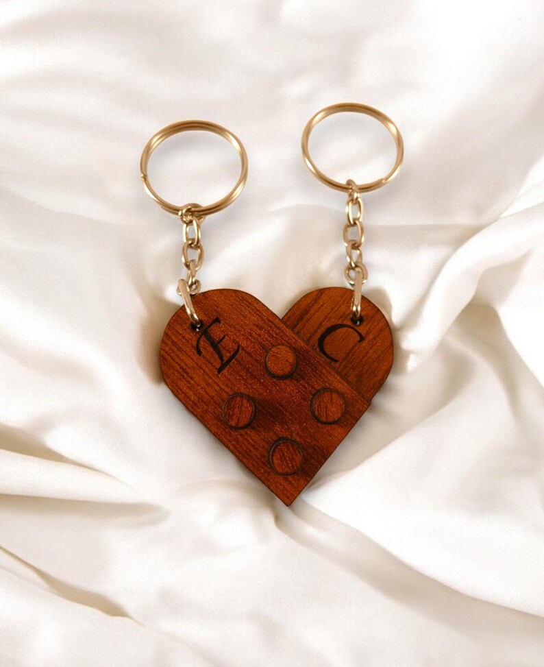 Puede incluir: Un par de llaveros de madera en forma de coraz&oacute;n con anillos y cadenas doradas. Los llaveros est&aacute;n grabados con las letras "L" y "C".