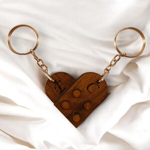 Puede incluir: Dos llaveros de madera en forma de coraz&oacute;n con cadenas y anillos dorados. Los llaveros est&aacute;n grabados con las letras "E" y "C".