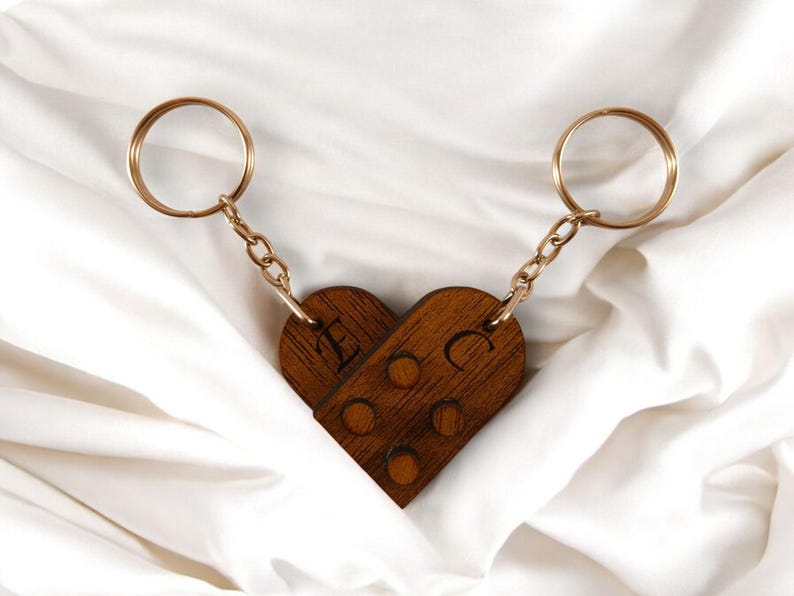 Puede incluir: Dos llaveros de madera en forma de coraz&oacute;n con cadenas y anillos dorados. Los llaveros est&aacute;n grabados con las letras "E" y "C".