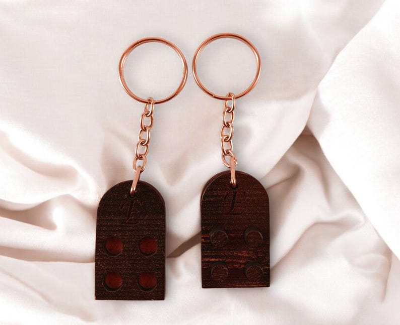 Puede incluir: Dos llaveros de madera marr&oacute;n con anillos y cadenas de metal dorado. Cada llavero tiene un n&uacute;mero diferente grabado. El llavero de la izquierda tiene el n&uacute;mero "1" grabado. El llavero de la derecha tiene el n&uacute;mero "2" grabado.