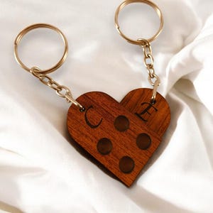 Puede incluir: Un llavero de madera con forma de coraz&oacute;n con las letras "C" y "E" grabadas. El llavero est&aacute; unido a dos llaveros de oro y una cadena.