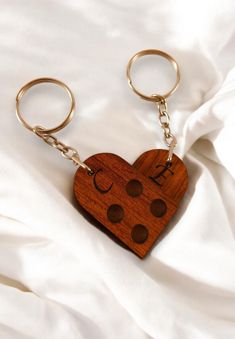 Puede incluir: Un llavero de madera con forma de coraz&oacute;n con las letras "C" y "E" grabadas. El llavero est&aacute; unido a dos llaveros de oro y una cadena.