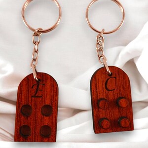 Puede incluir: Dos llaveros de madera con un anillo y una cadena de metal dorado. Los llaveros tienen forma de casita peque&ntilde;a con una letra 'E' y 'C' grabadas en la parte delantera. Cada llavero tiene cuatro peque&ntilde;os c&iacute;rculos en la parte delantera.