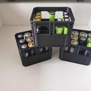 Könnte beinhalten: Drei schwarze Plastik-Batterie-Aufbewahrungskisten mit einer Vielzahl von AA- und AAA-Batterien im Inneren. Die Kisten sind übereinander gestapelt.